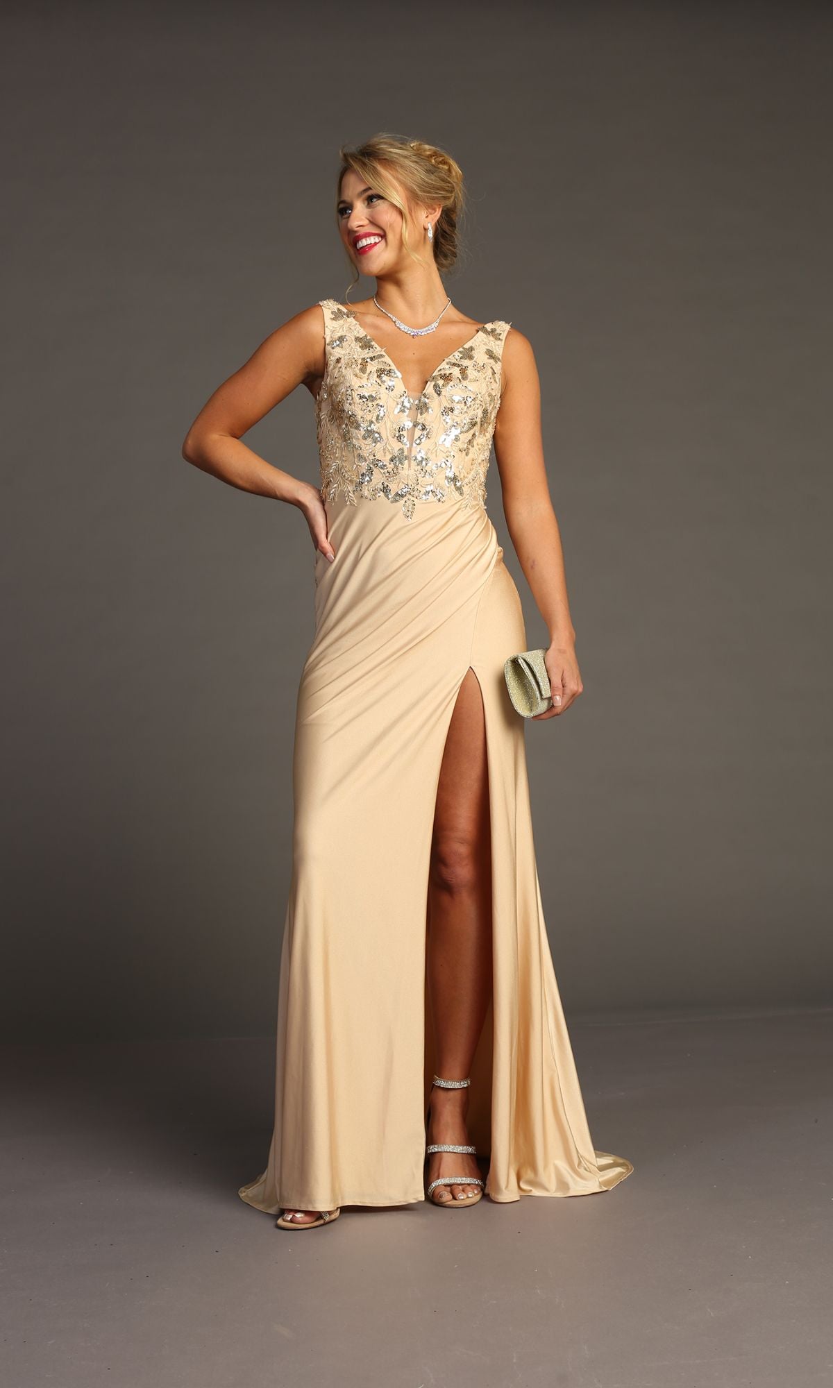 Woman in the Sequin-Bodice Long Prom Dress: Chicas YG5032, a sleeveless beige gown with a high slit and sparkling bodice, paired with strappy heels and a clutch, standing against a plain background.